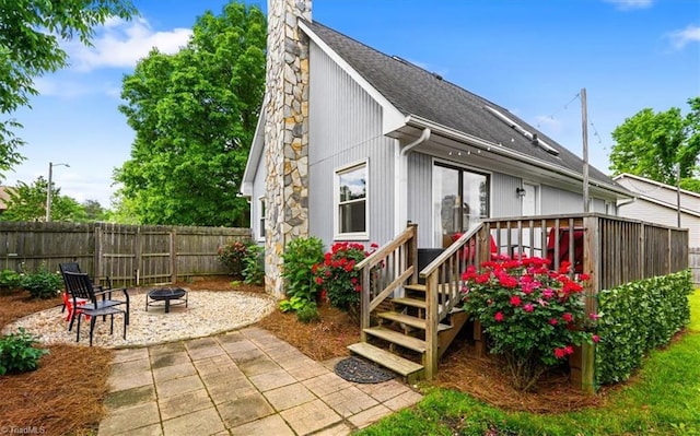 rear view of property with roof with shingles, a patio area, fence, a fire pit, and a chimney