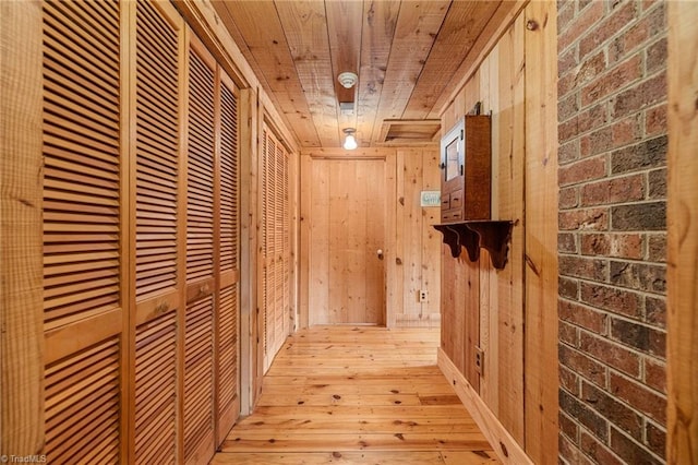 corridor featuring wooden ceiling, light hardwood / wood-style floors, wooden walls, and brick wall