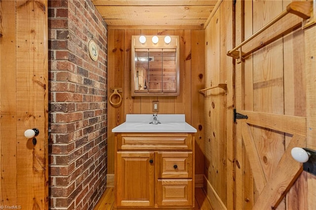 bathroom featuring vanity, wood-type flooring, wooden walls, wood ceiling, and brick wall