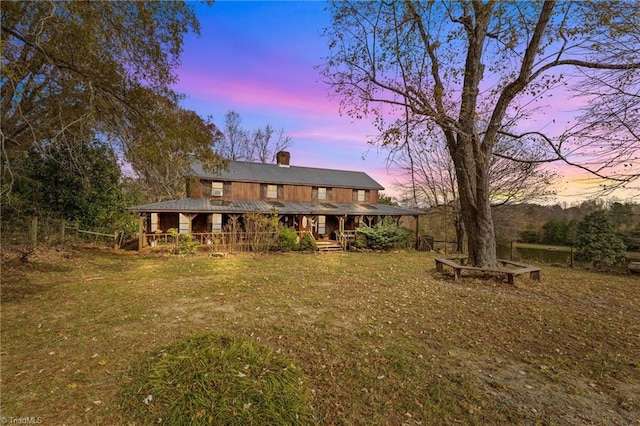 back house at dusk featuring covered porch and a yard