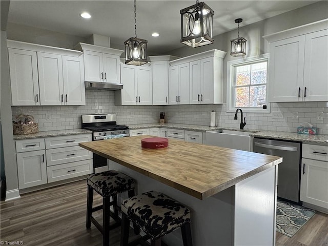 kitchen featuring wooden counters, appliances with stainless steel finishes, a center island, a kitchen bar, and white cabinets