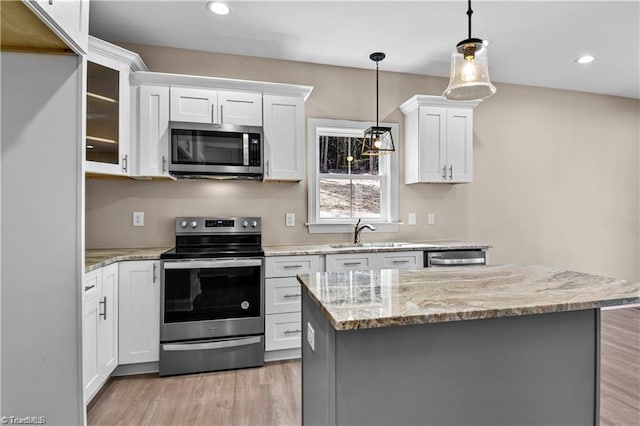 kitchen featuring pendant lighting, appliances with stainless steel finishes, a kitchen island, light stone counters, and white cabinetry