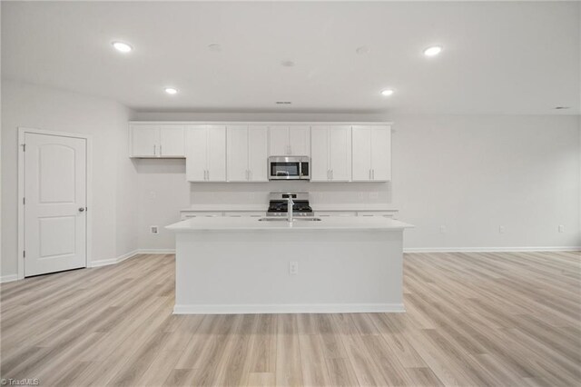 5365 Roshni Ter, Mcleansville, NC 27301 - kitchen featuring stainless steel microwave, an island with sink, white cabinetry, light countertops, and light wood finished floors