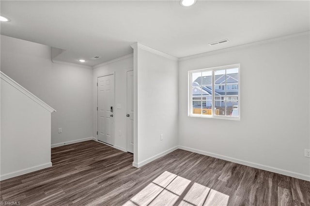 empty room with crown molding, wood finished floors, baseboards, and visible vents