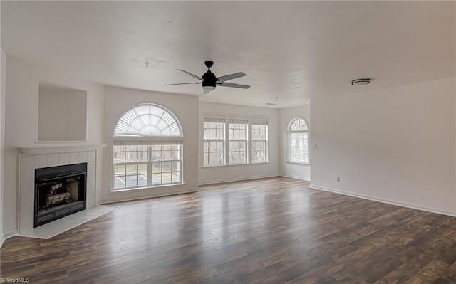 unfurnished living room with baseboards, a ceiling fan, wood finished floors, and a tiled fireplace