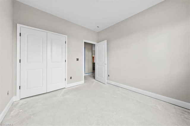 unfurnished bedroom with a closet, concrete floors, and baseboards