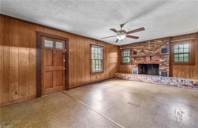 unfurnished living room with ceiling fan, a textured ceiling, a fireplace, and wood walls