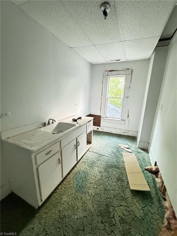 interior space featuring a paneled ceiling, white cabinetry, sink, and dark carpet