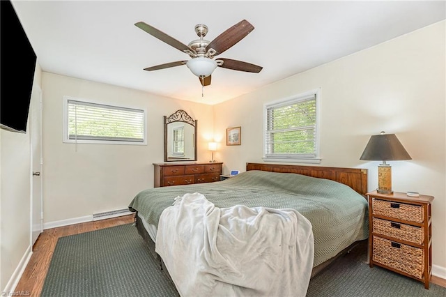 bedroom featuring a baseboard heating unit, multiple windows, wood finished floors, and baseboards
