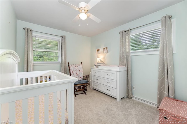 bedroom with a nursery area, a ceiling fan, multiple windows, and light colored carpet
