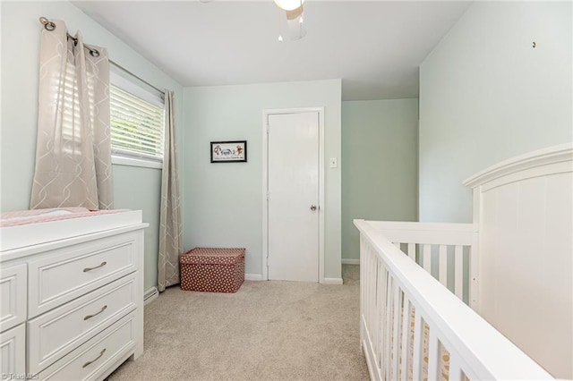 bedroom featuring a crib, a ceiling fan, light colored carpet, and baseboards