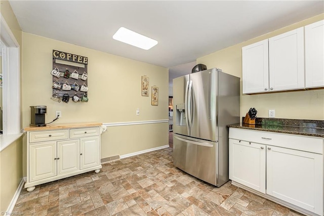 kitchen featuring white cabinets, baseboards, stone finish floor, and stainless steel fridge with ice dispenser