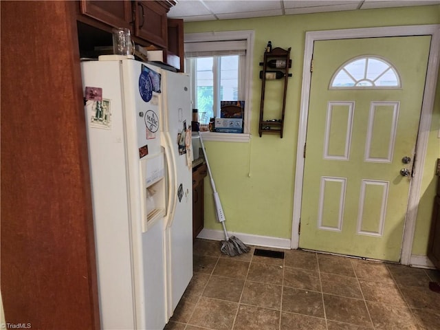 kitchen with a paneled ceiling, plenty of natural light, dark tile patterned floors, and white fridge with ice dispenser