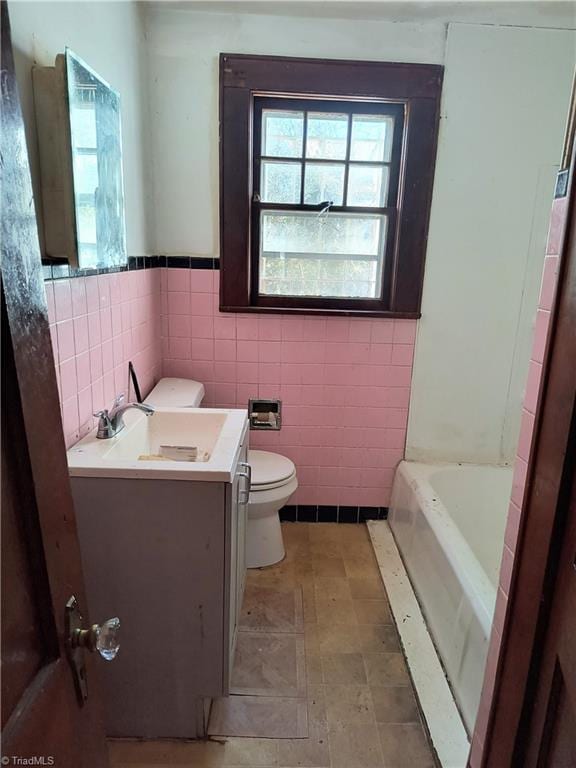 bathroom featuring vanity, a tub, tile walls, and toilet