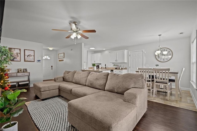 living room featuring ceiling fan with notable chandelier, dark wood-type flooring, and sink