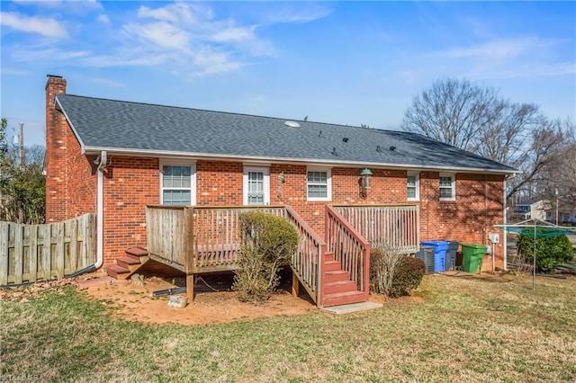 back of house with roof with shingles, a yard, a chimney, fence, and a wooden deck