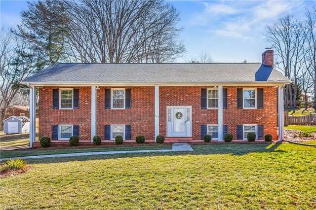 split foyer home featuring an outbuilding, brick siding, a chimney, a storage unit, and a front lawn