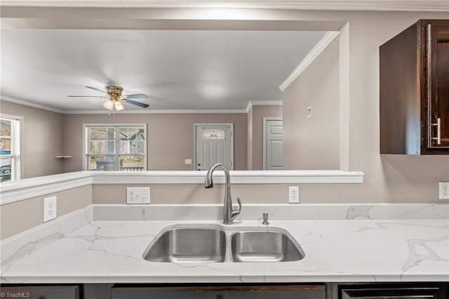 kitchen featuring light stone counters, dark brown cabinetry, a sink, a ceiling fan, and crown molding