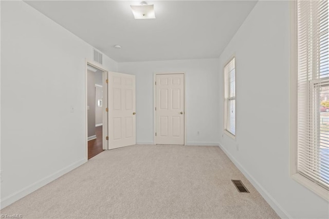 unfurnished room with a wealth of natural light, visible vents, and light colored carpet