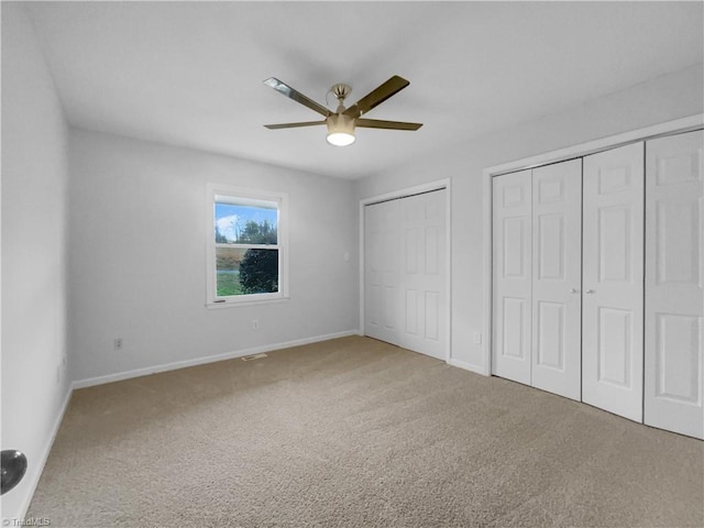 unfurnished bedroom featuring baseboards, carpet floors, a ceiling fan, and multiple closets