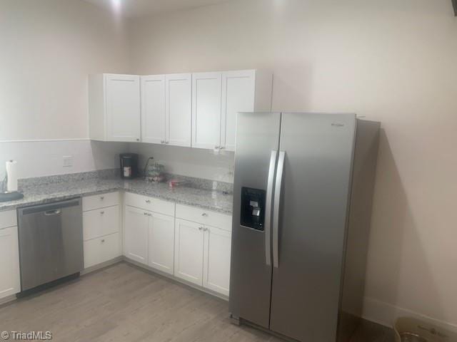 kitchen with white cabinets, light hardwood / wood-style floors, light stone counters, and appliances with stainless steel finishes