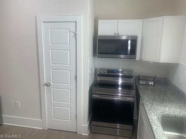 kitchen with stone counters, white cabinets, sink, hardwood / wood-style flooring, and appliances with stainless steel finishes