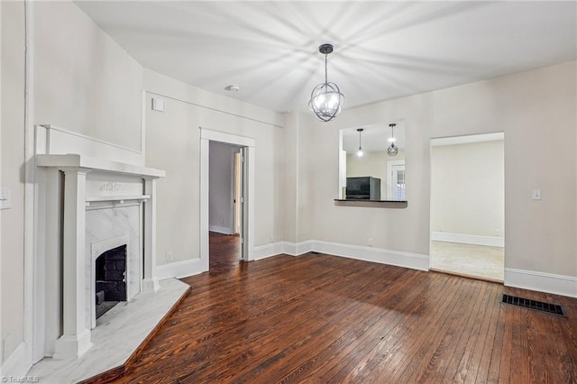 unfurnished living room with a premium fireplace, wood-type flooring, and an inviting chandelier