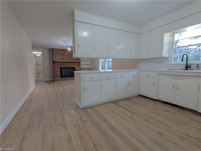 kitchen with a fireplace, sink, white cabinets, and light hardwood / wood-style flooring