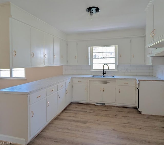 kitchen with white cabinets, backsplash, light hardwood / wood-style floors, and sink