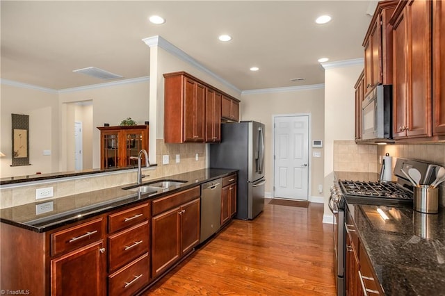 kitchen with dark wood-type flooring, dark stone counters, appliances with stainless steel finishes, a peninsula, and a sink