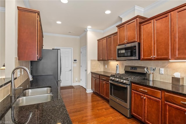 kitchen with a sink, dark wood-style floors, stainless steel appliances, dark stone counters, and crown molding