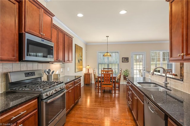 kitchen with wood finished floors, dark stone countertops, stainless steel appliances, and a sink