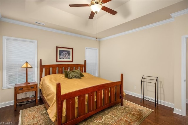 bedroom featuring wood finished floors, baseboards, visible vents, a tray ceiling, and crown molding