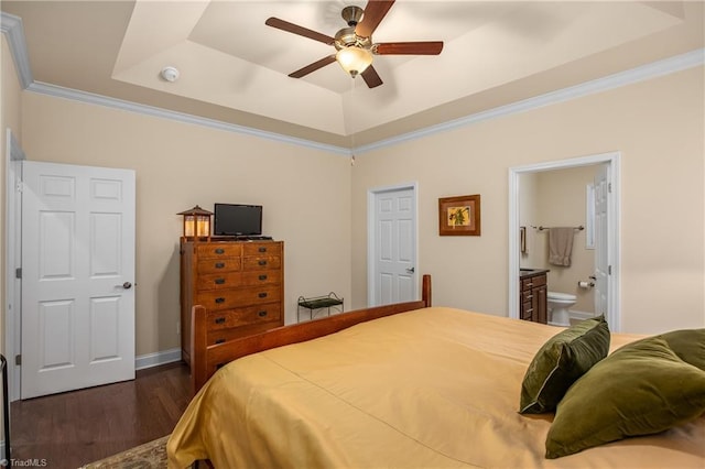 bedroom with dark wood-style floors, a tray ceiling, ceiling fan, ornamental molding, and connected bathroom