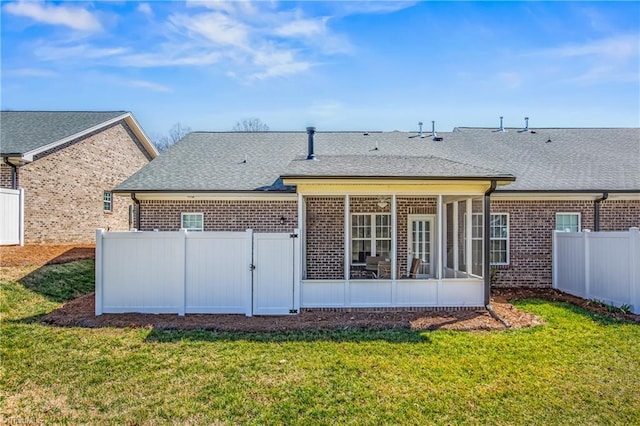 rear view of house with a fenced backyard, brick siding, a yard, and a sunroom