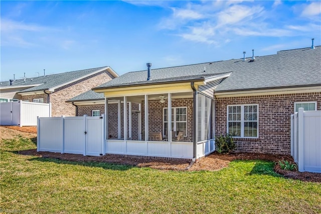 rear view of house with fence, a lawn, brick siding, and a sunroom