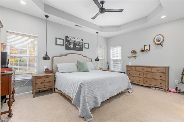 carpeted bedroom with multiple windows, a tray ceiling, and ceiling fan