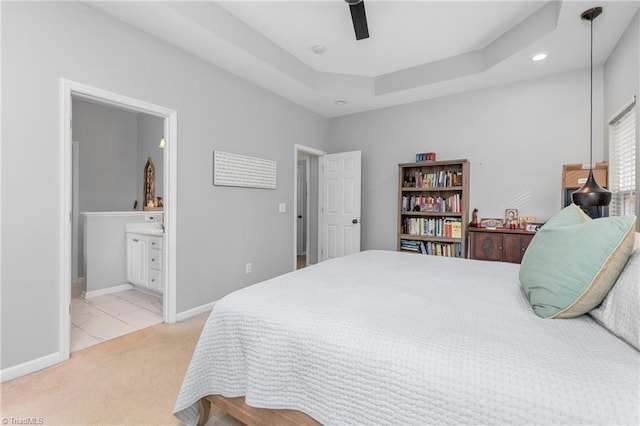 bedroom featuring light carpet, connected bathroom, a tray ceiling, and ceiling fan