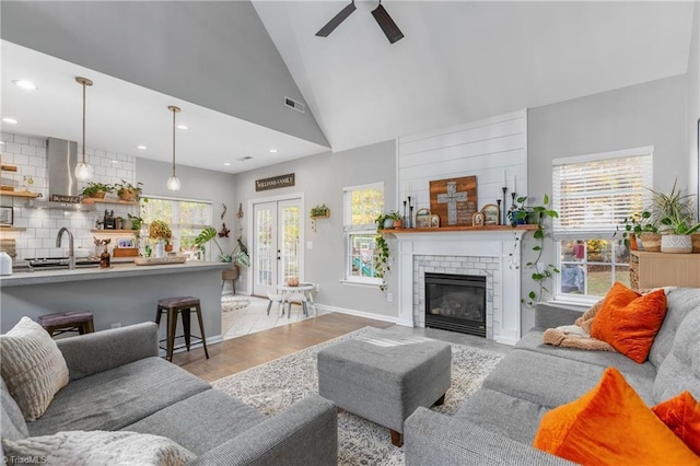 living room featuring french doors, ceiling fan, sink, light hardwood / wood-style flooring, and a fireplace