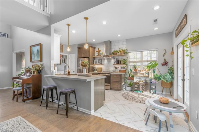 kitchen with wall chimney exhaust hood, hanging light fixtures, stainless steel appliances, kitchen peninsula, and a breakfast bar area