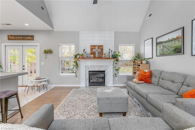 living room with a tile fireplace, french doors, light wood-type flooring, and vaulted ceiling