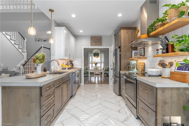 kitchen featuring tasteful backsplash, stainless steel appliances, sink, wall chimney range hood, and hanging light fixtures