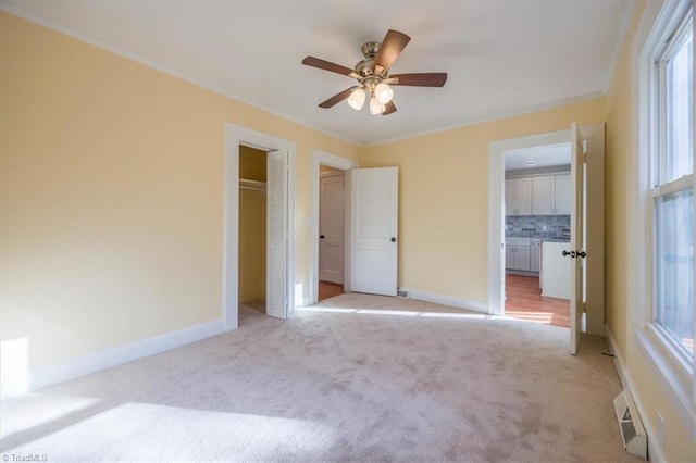 unfurnished bedroom with a closet, ceiling fan, crown molding, and light colored carpet