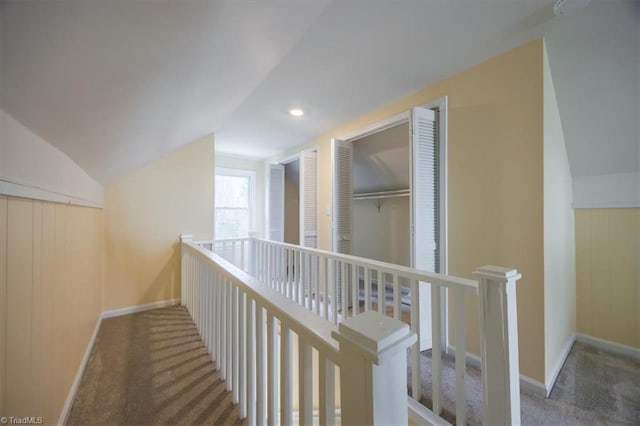 corridor featuring carpet flooring, wood walls, and lofted ceiling