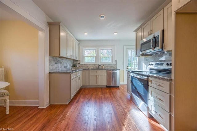 kitchen with white cabinets, decorative backsplash, light stone countertops, light wood-type flooring, and stainless steel appliances