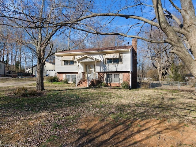 split foyer home featuring brick siding, a chimney, fence, and a front yard