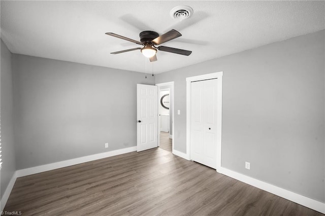 unfurnished bedroom with a closet, visible vents, a ceiling fan, wood finished floors, and baseboards