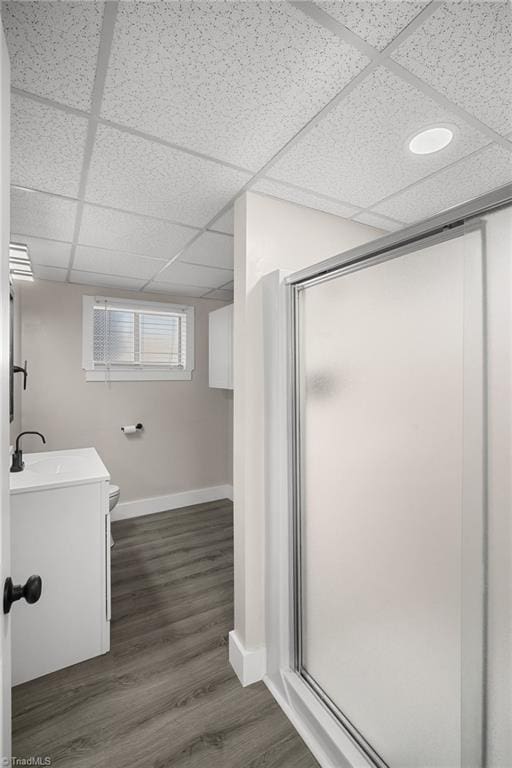 bathroom featuring a paneled ceiling, toilet, wood finished floors, vanity, and a stall shower