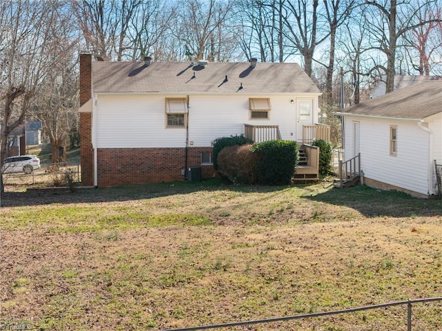 back of house featuring a yard, brick siding, a chimney, and central AC unit