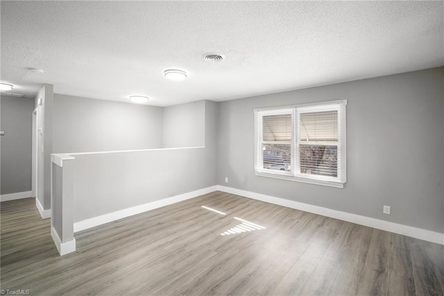 spare room with wood finished floors, visible vents, and baseboards